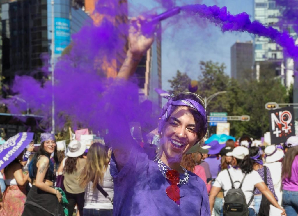 A vibrant public demonstration in Mexico City showcasing female empowerment with purple smoke.